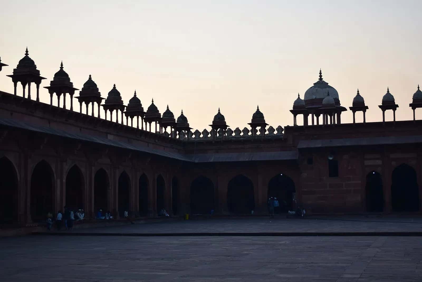 Gün batımında Fatehpur Sikri Cuma Mescidi'nin revaklı avlusu ve küçük kubbeli köşklerin silueti