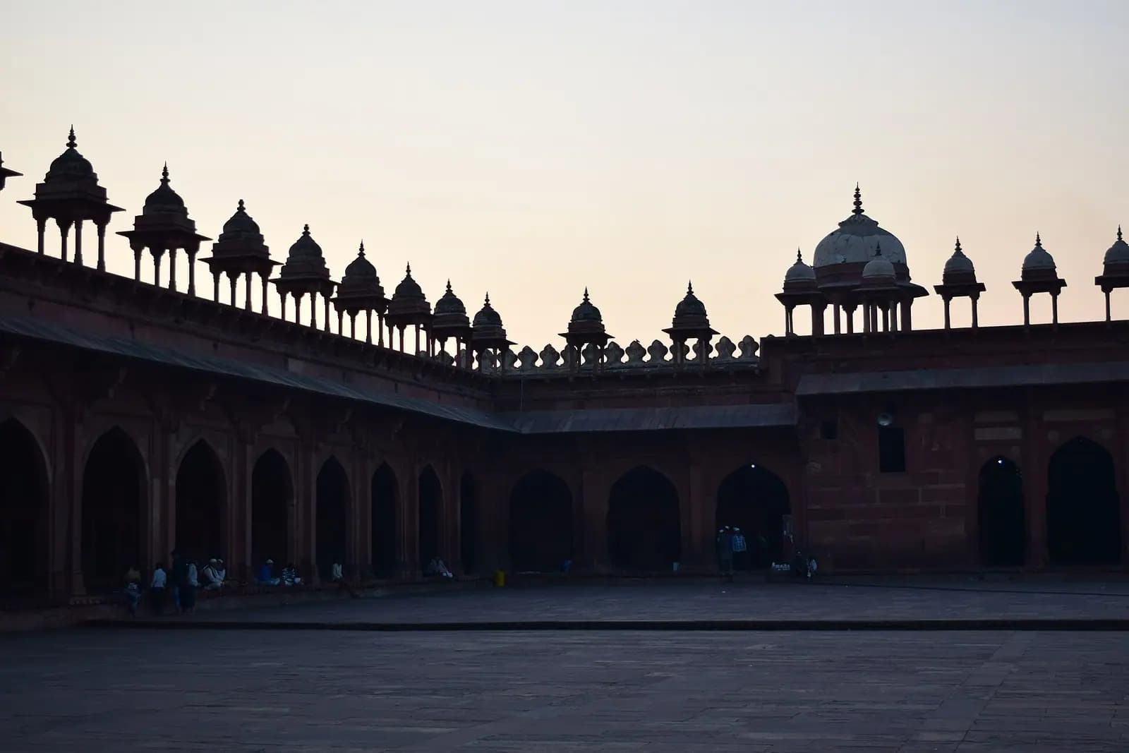 Gün batımında Fatehpur Sikri Cuma Mescidi'nin revaklı avlusu ve küçük kubbeli köşklerin silueti