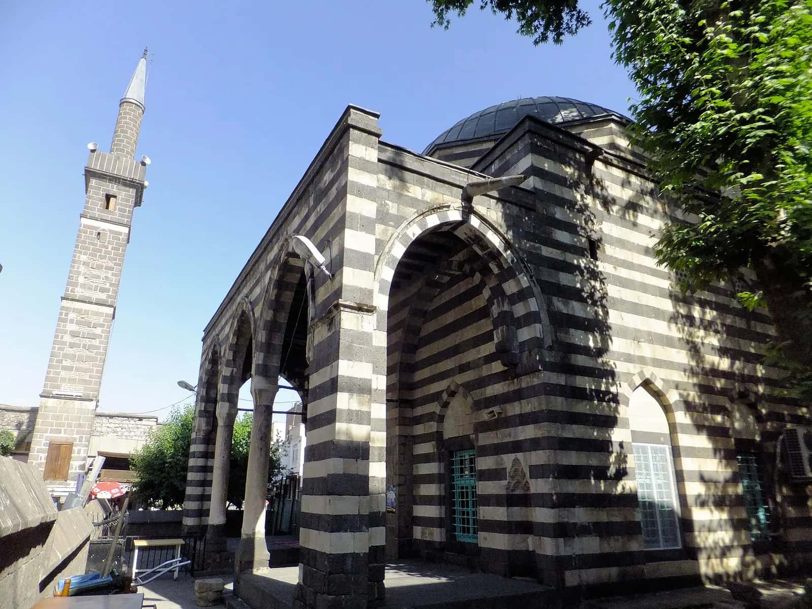 Şeyh Mutahhar Camii'nin siyah-beyaz taş sıralı cephesi ve yanında yükselen minare
