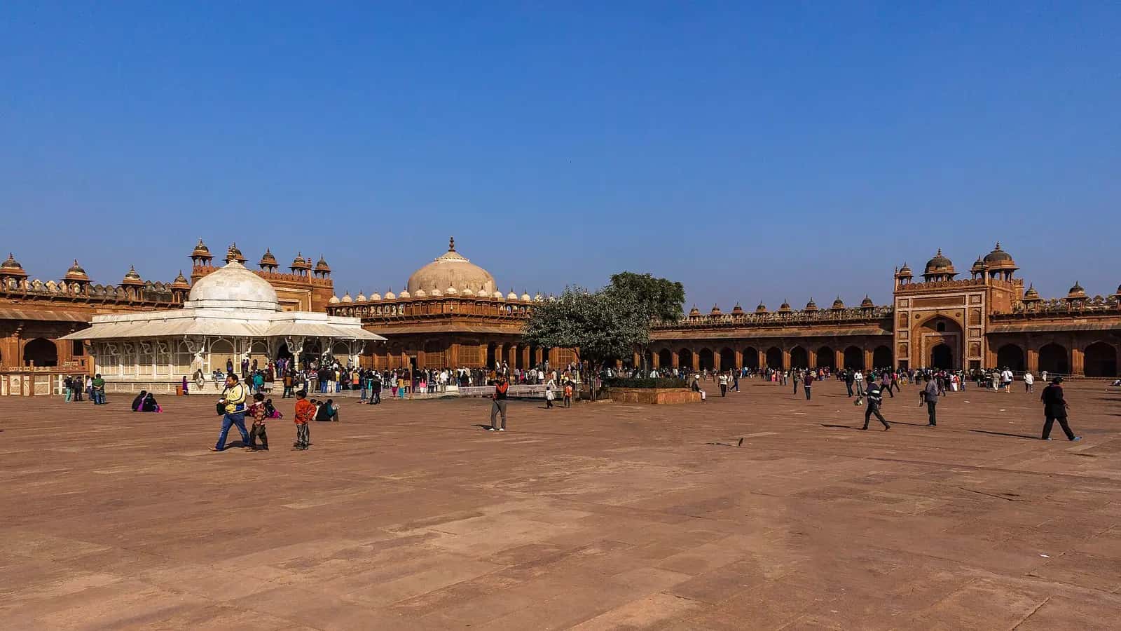 Fatehpur Sikri Cuma Mescidi'nin geniş avlusu, beyaz mermer Selîm Çiştî Türbesi ve arkadaki kubbeli ibadet mekânı