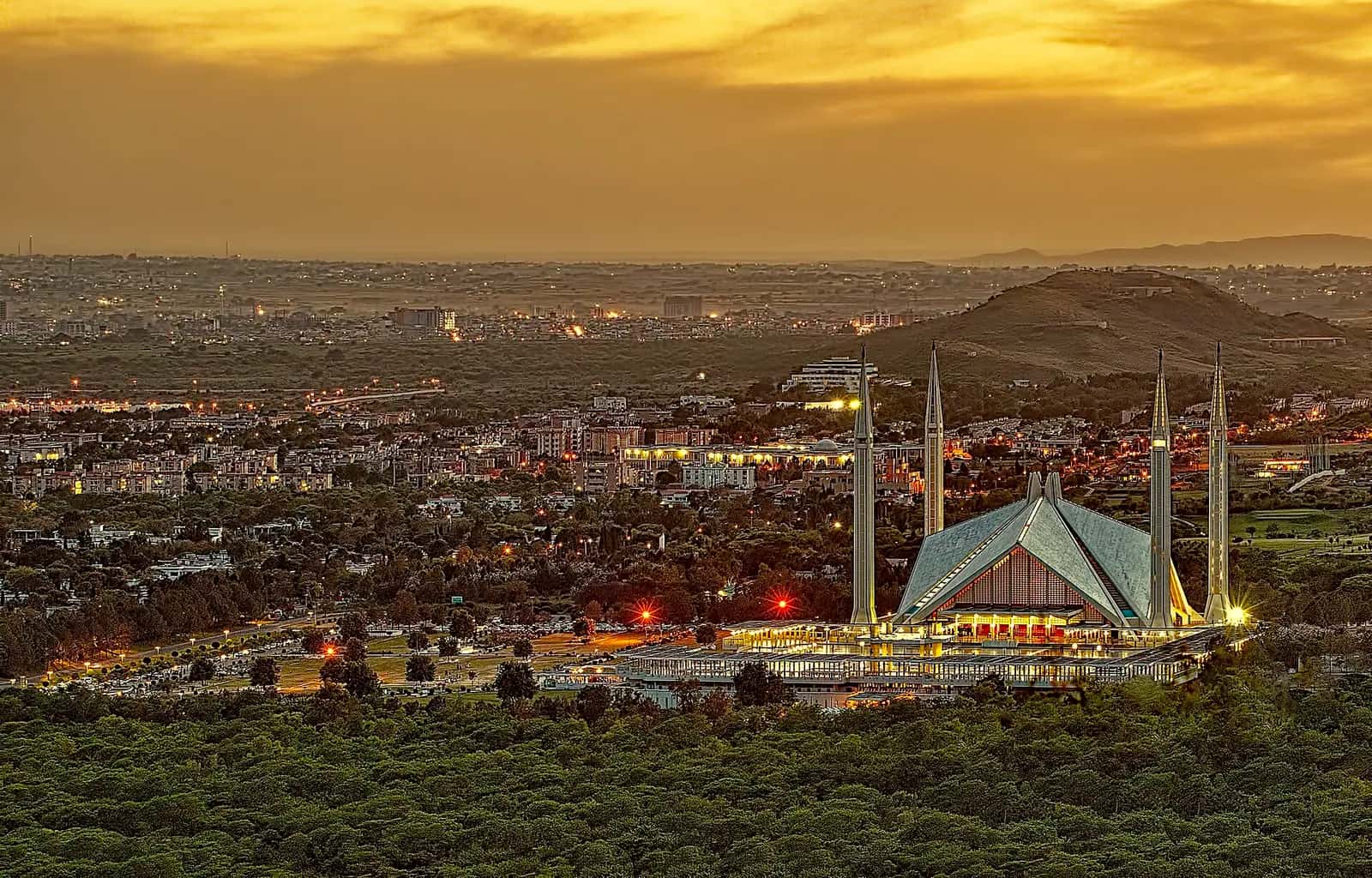 Akşam ışığında İslamabad manzarası önünde dört ince minaresi ve üçgen çatı kabuğuyla Faysal Camii