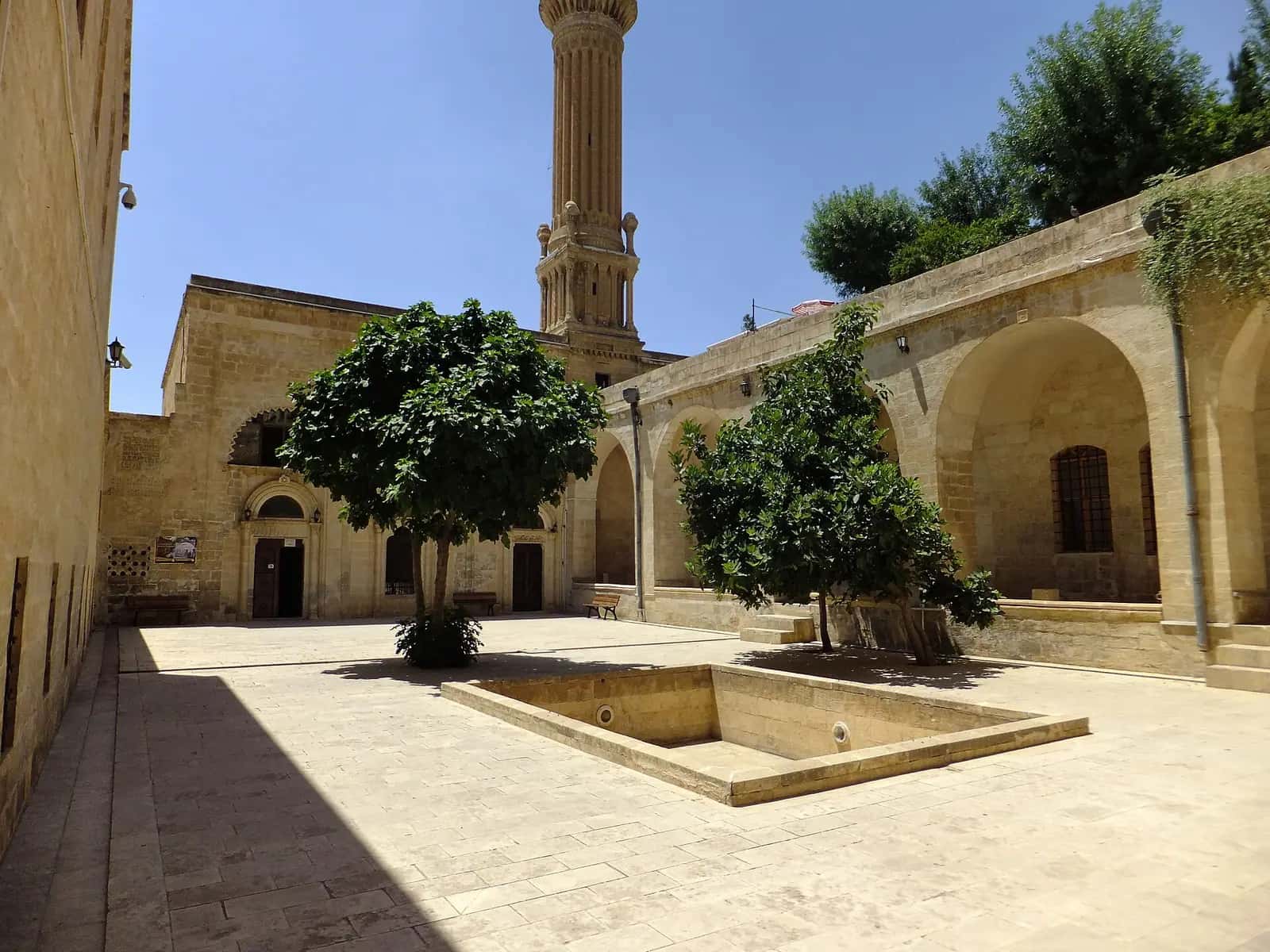 Şehidiye Medresesi'nin havuzlu avlusu, ağaçları ve arkada minaresi