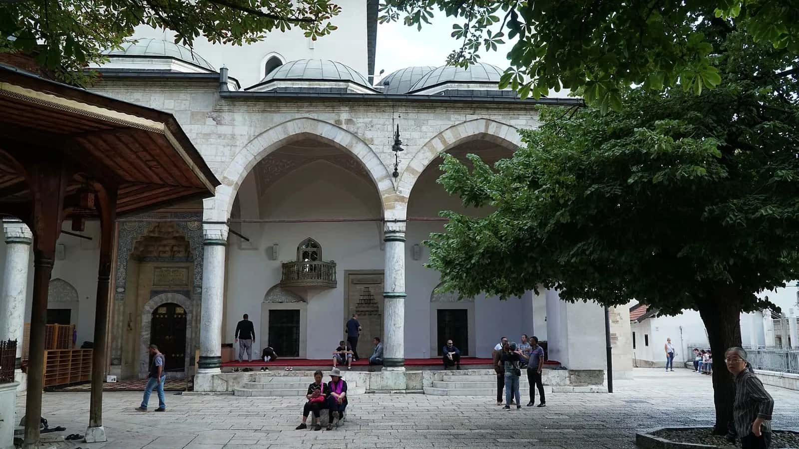 Gazi Hüsrev Bey Camii'nin revaklı son cemaat yeri, kubbeleri ve avludaki ağaçlar