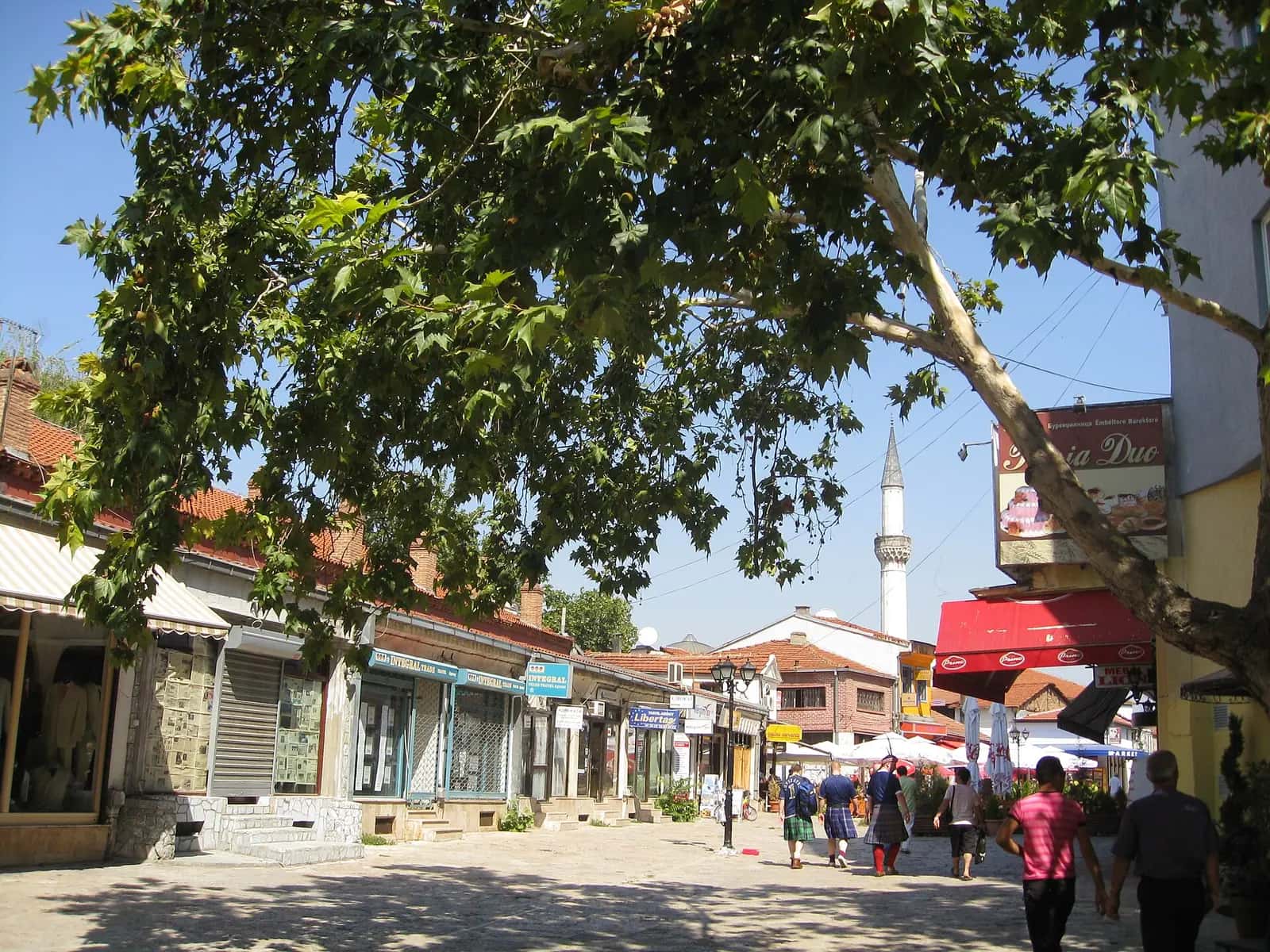 Üsküp Eski Çarşı'da dükkânlarla çevrili taş döşeli sokak ve arkada yükselen minare